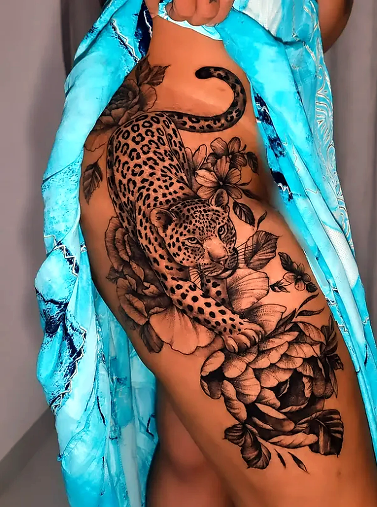 Tatuagem de onça com flores na lateral do quadril