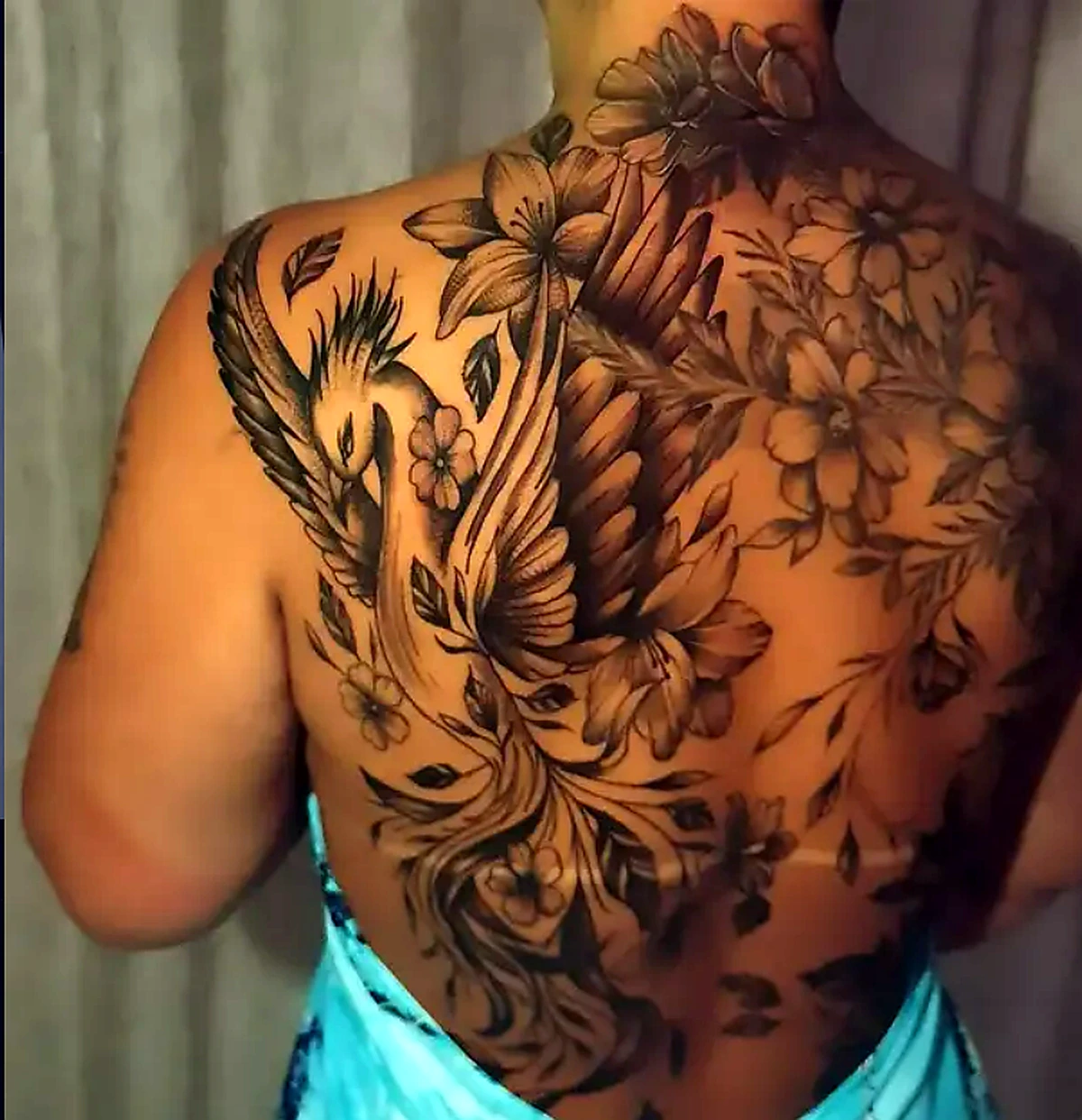 Tatuagem de fênix e composição botânica nas costas